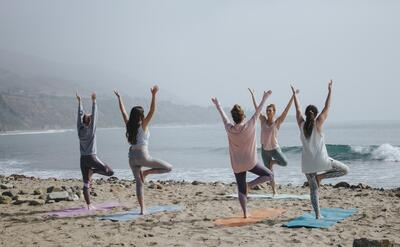 Five women practicing yoga on the beach.