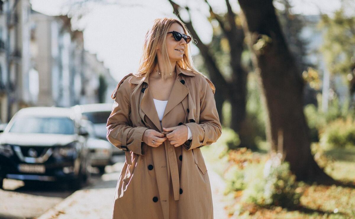 Young blonde woman in beige coat walking in the street