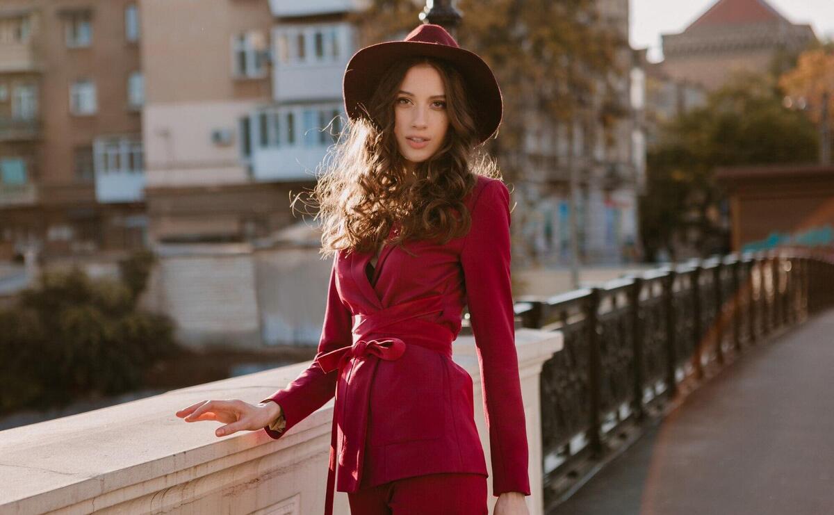 Happy beautiful stylish woman in purple suit walking in city street, spring summer autumn season fashion trend wearing hat, holding purse