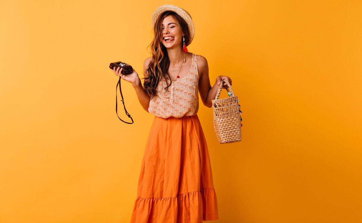 Blissful lady in trendy summer clothes posing with camera on yellow. Positive beautiful girl in hat chilling in studio.