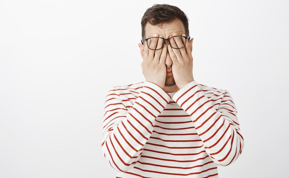 Portrait of hardworking tired adult male in striped pullover and glasses, rubbing face with palms, feeling tired and resting after hard day