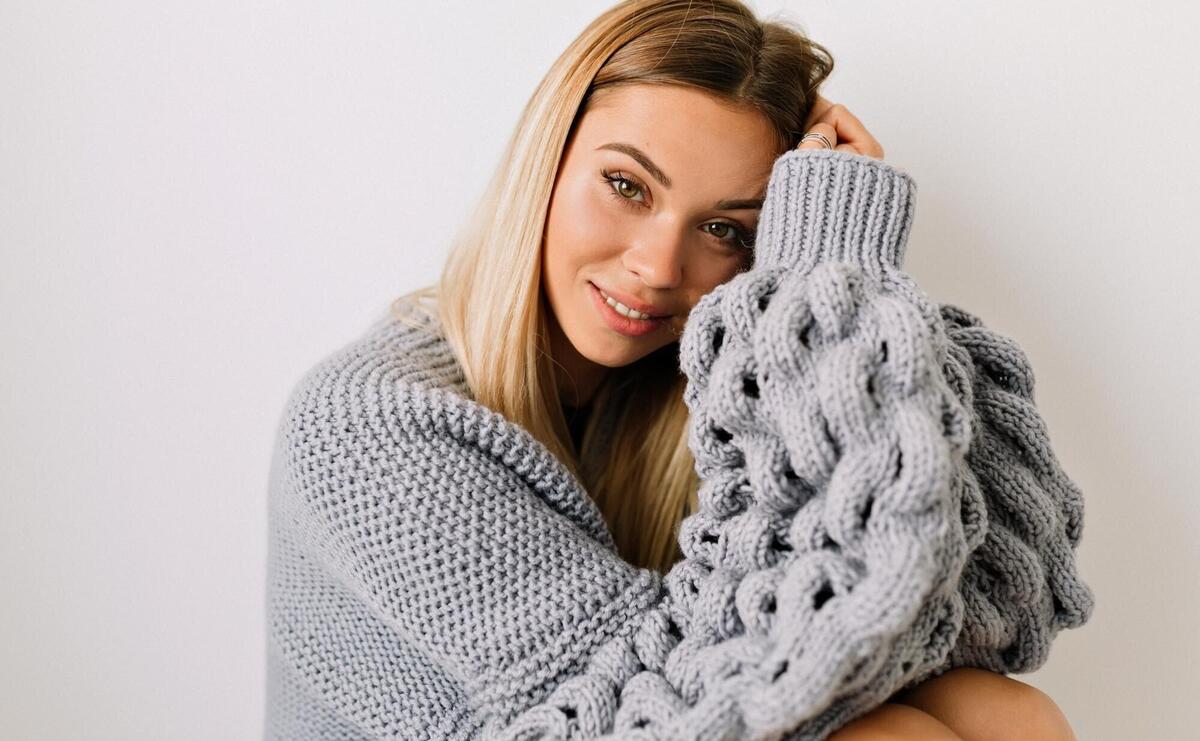 Inside portrait of adorable lovely woman with blond hair wearing knitted pullover is posing over isolated background with romantic smile Beautiful woman is posing during photoshoot