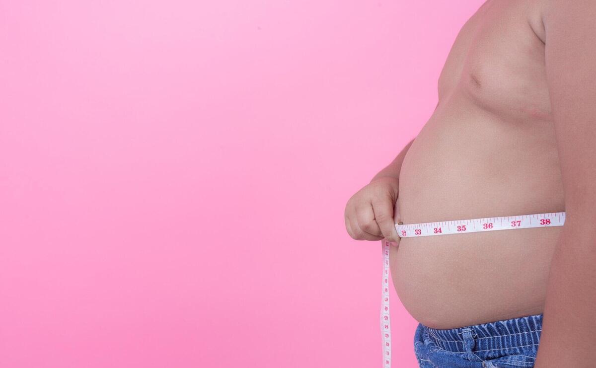 Obese boy who is overweight on a pink background.