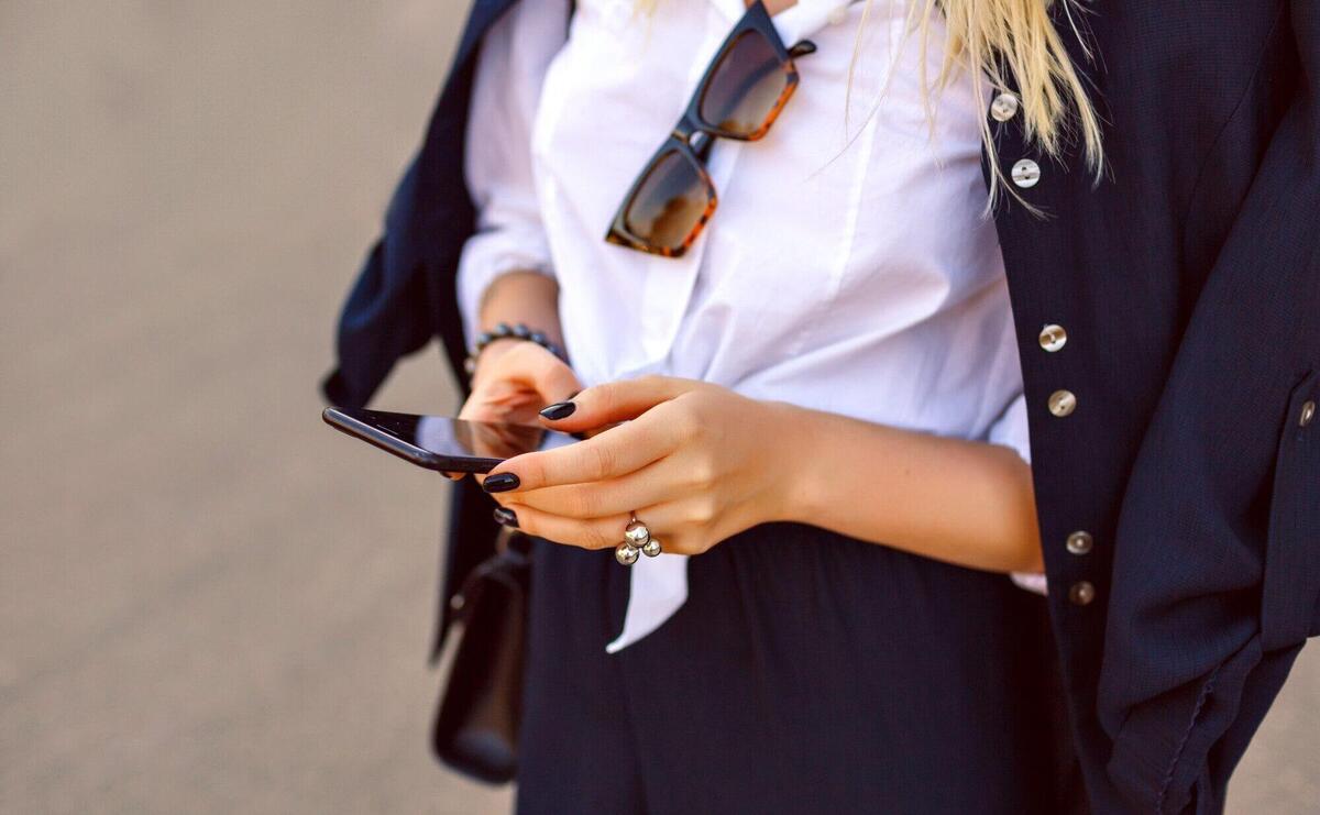 Fashion close up details of woman holding her smartphone and tap massage, official business suit and luxury trendy accessories, focus on hands.