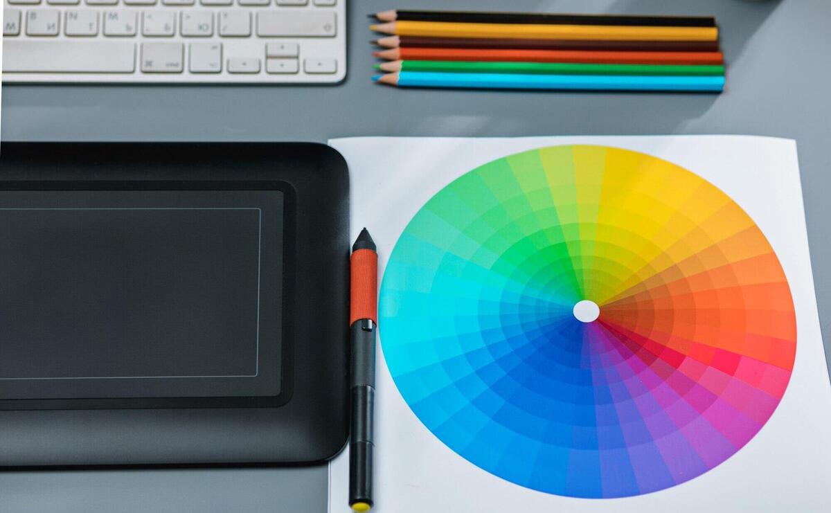 gray desk with laptop, notepad with blank sheet, pot of flower, stylus and tablet for retouching