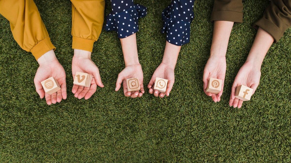 Hand's holding social media app icons wooden blocks on green grass