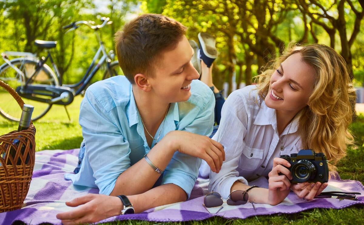 The attractive young couple using a compact photo camera at a picnic in a park.