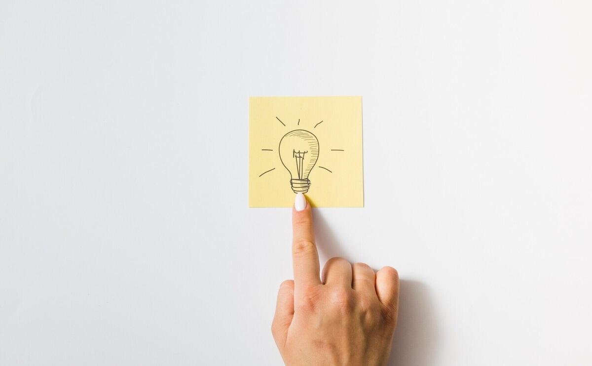 Close-up of a person touching finger on drawn light bulb over the sticky note