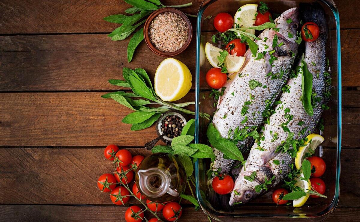 Two raw seabass in a baking dish with spices on an old wooden table. Top view