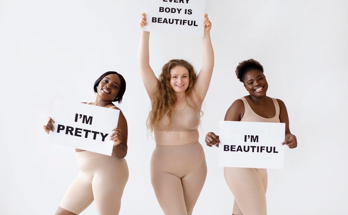 Three women holding placards with body positivity statements