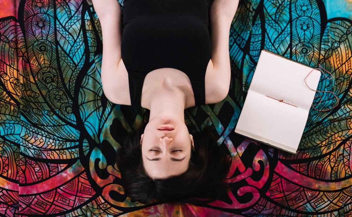 Overhead view of eyes closed woman lying near open blank book on blanket