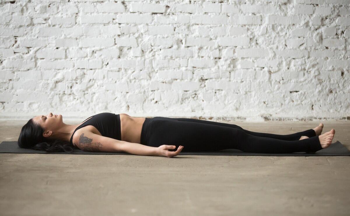 Young yogi attractive woman in Savasana pose, white loft backgro