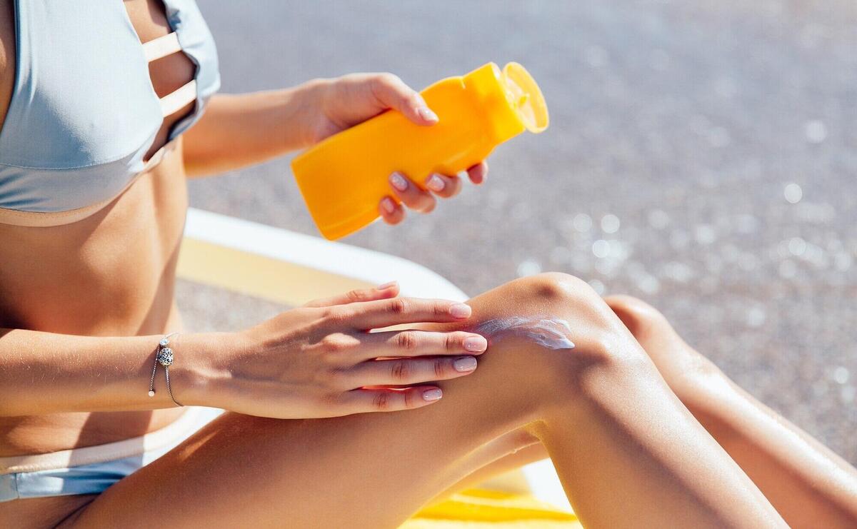 Close-up view of female hands applying sunscreen on her leg, on the beach. Sunbathing.