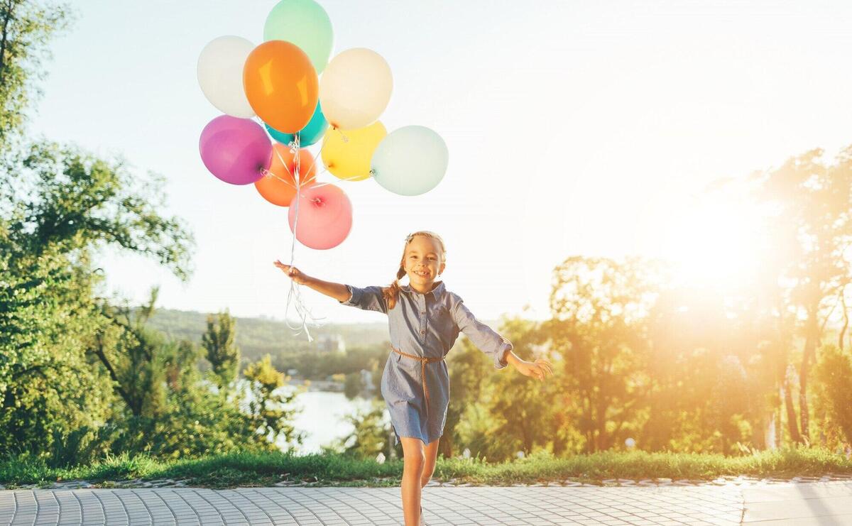 Happy girl holding colorful balloons in the city park