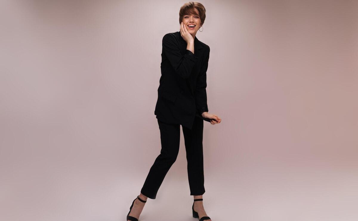 Stylish lady in suit laughing on isolated background. Full-lenght portrait of woman dressed in black jacket and pants posing and smiling on white backdrop