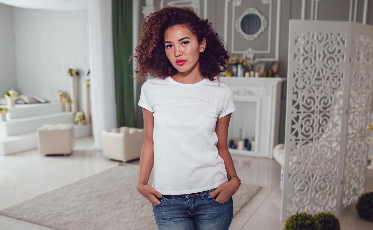 A woman stands in a room with a white wall behind her.