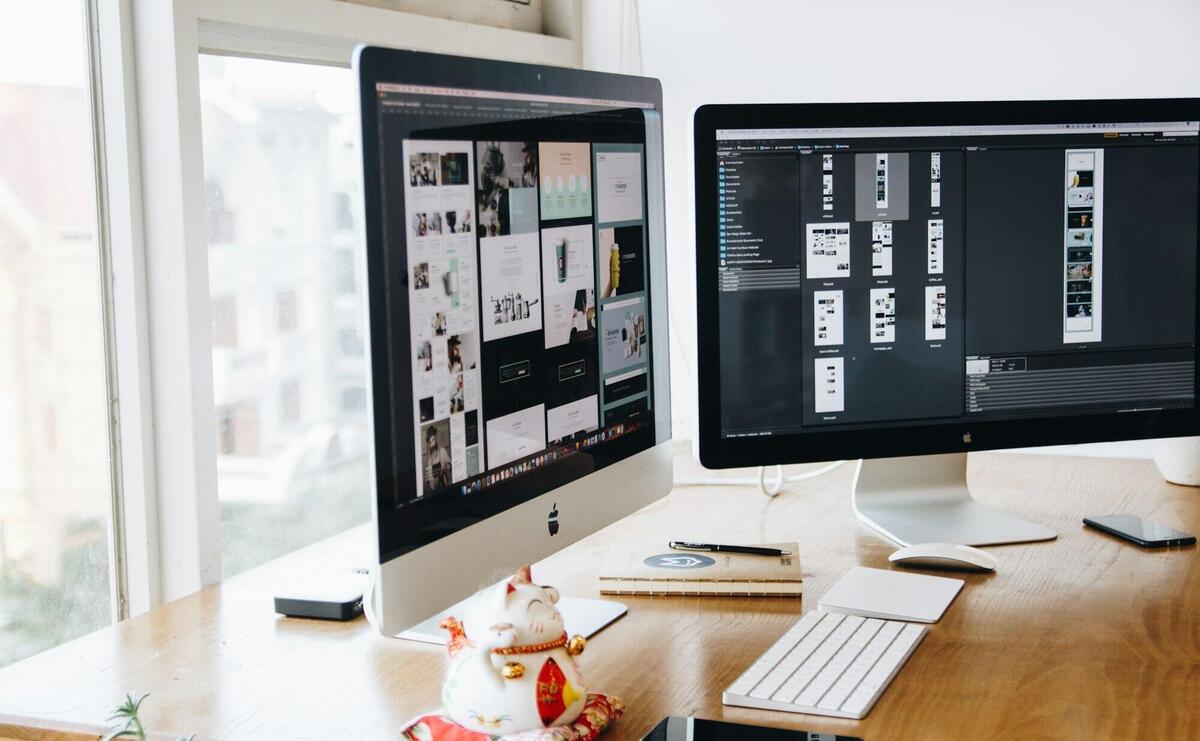 A sleek modern office setup featuring dual monitors, Apple devices, and creative decor in an indoor workspace.