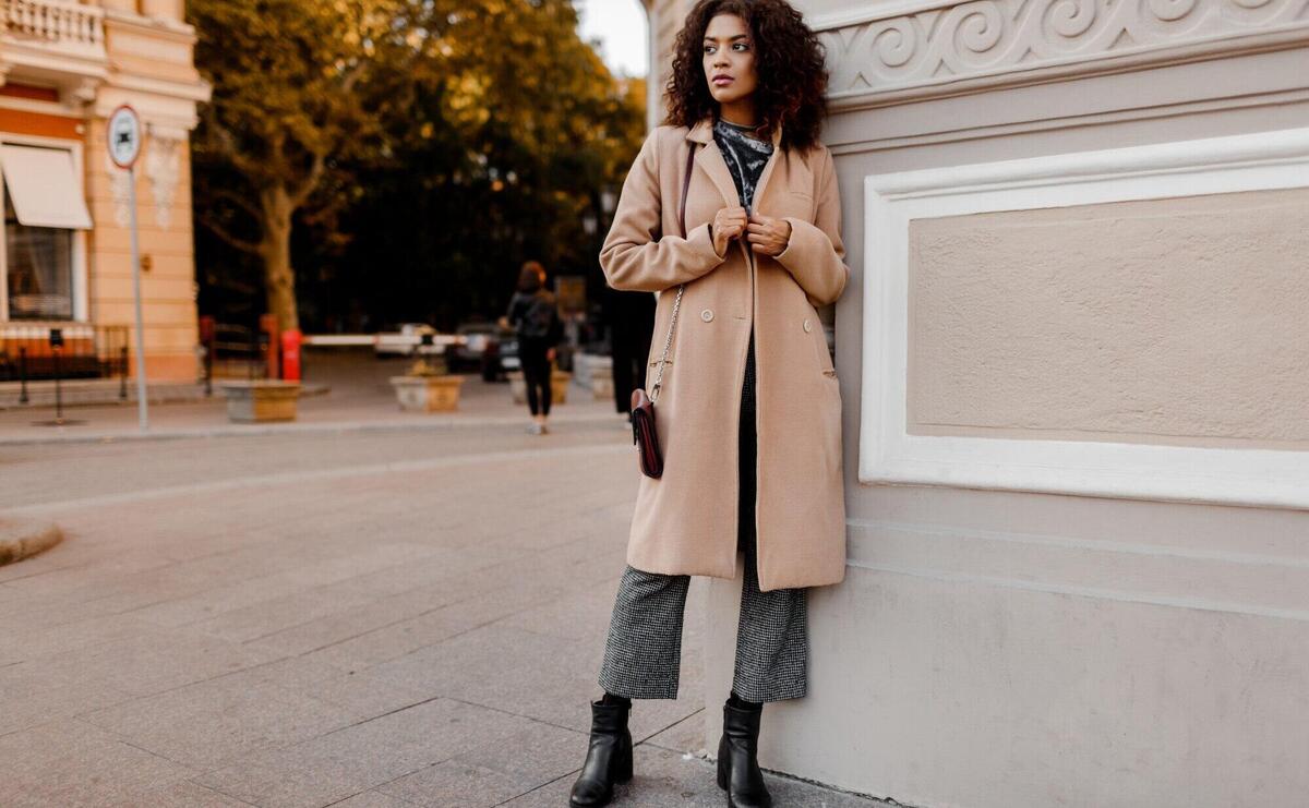 Outdoor fashion portrait of glamour sensual young stylish black lady wearing trendy fall outfit, grey velvet sweater and beige wool coat.