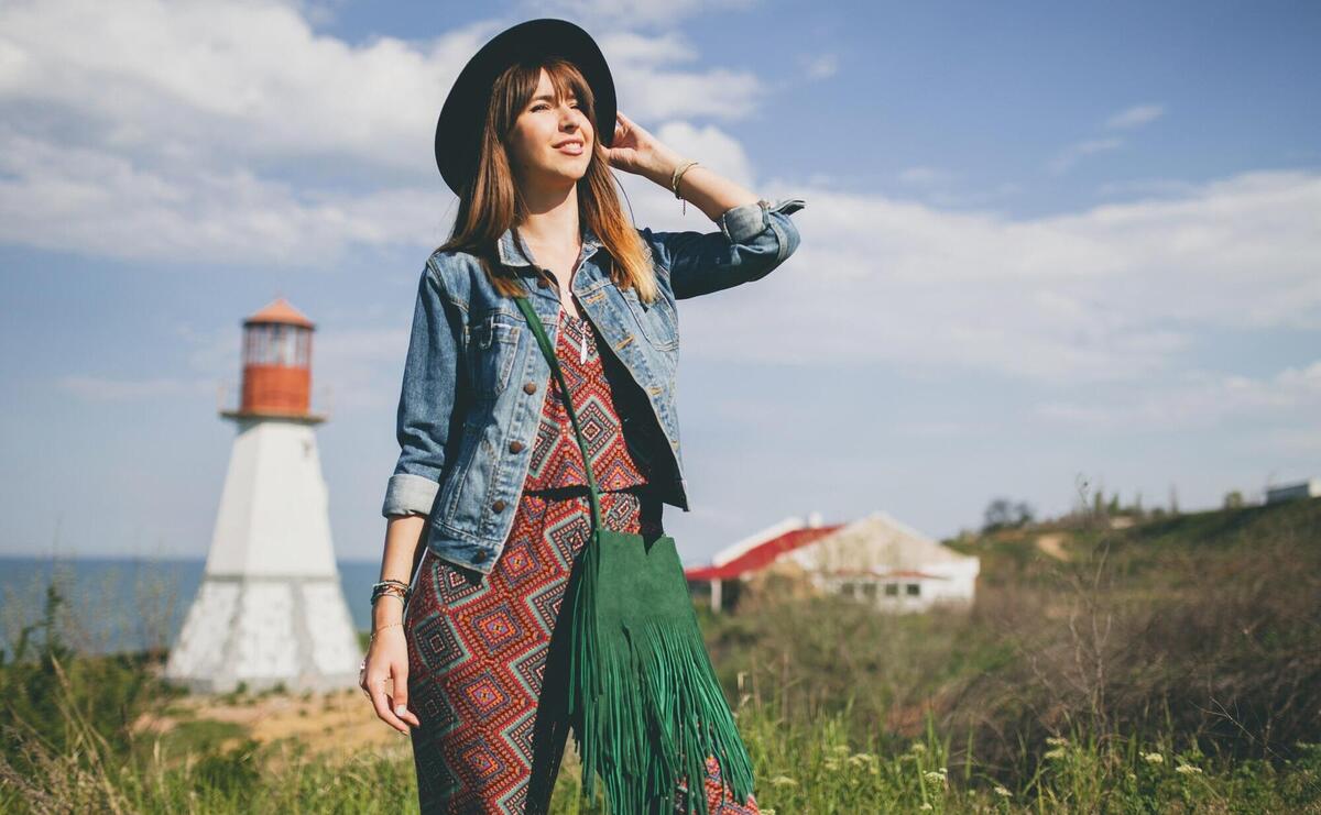 Young woman in nature, lighthouse, bohemian outfit, denim jacket, black hat, smiling, happy, summer, stylish accessories