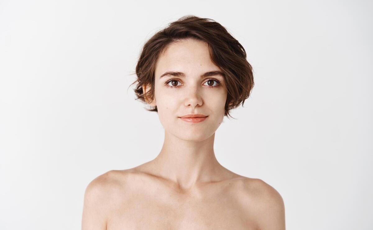 Skincare Young caucasian woman with short hair and naked body smiling at camera Girl with hydrated skin looking happy after applying daily care facial cream white background