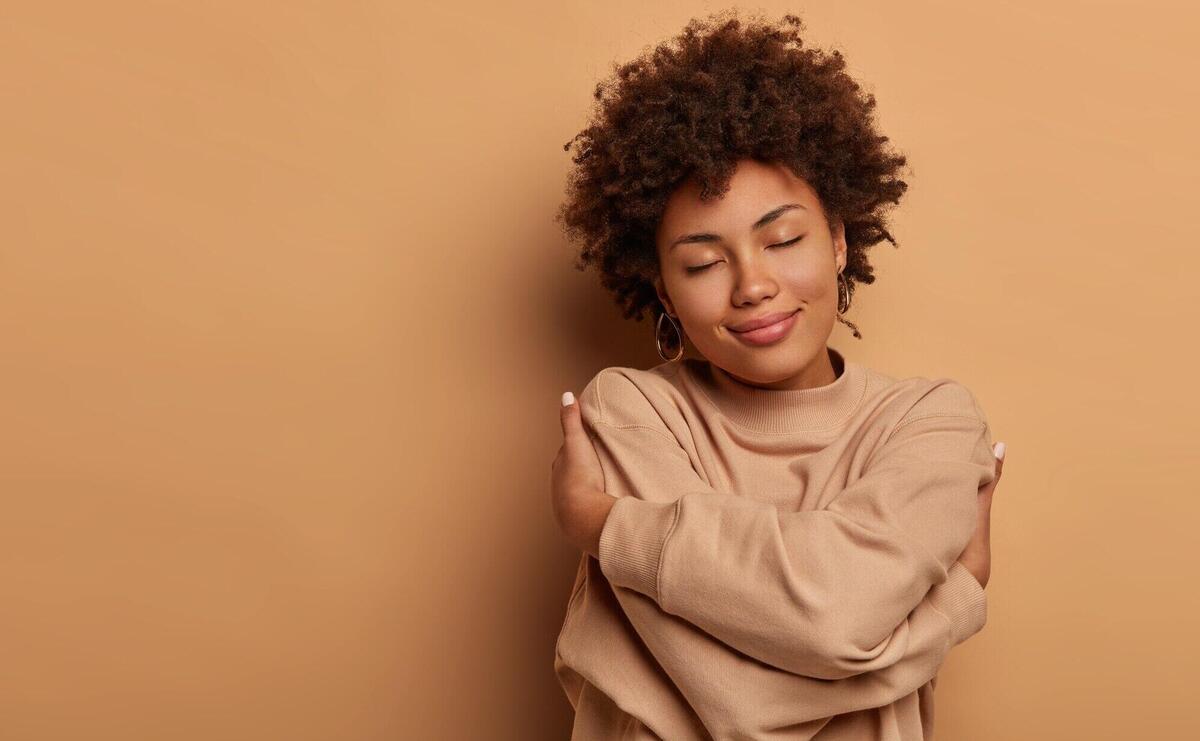 Love yourself, self acceptance. Gentle lovely Afro American woman crosses hands and embraces own body, tilts head and closes eyes