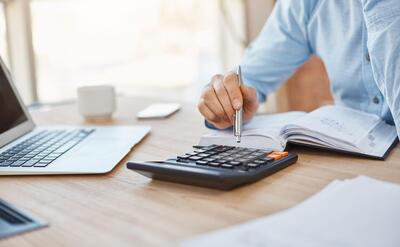 Close up detail of professional serious accountant sitting in light office, checking company finance profits on calculator