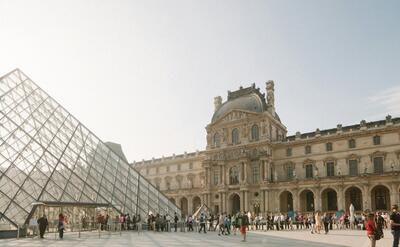 Stunning view of the Louvre Museum's glass pyramid entrance with tourists in the courtyard in Paris, France.