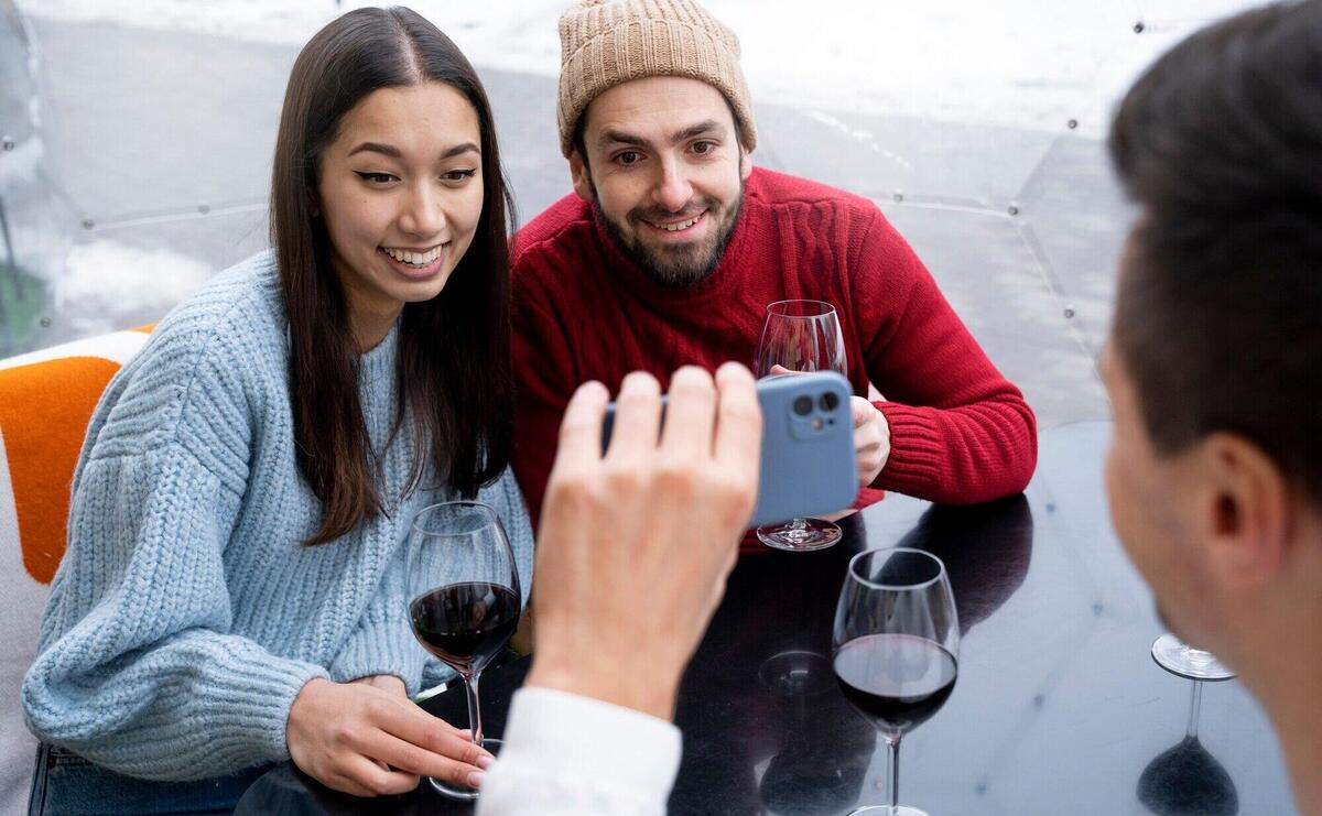 Man showing friends smartphone screen while having wine during reunion