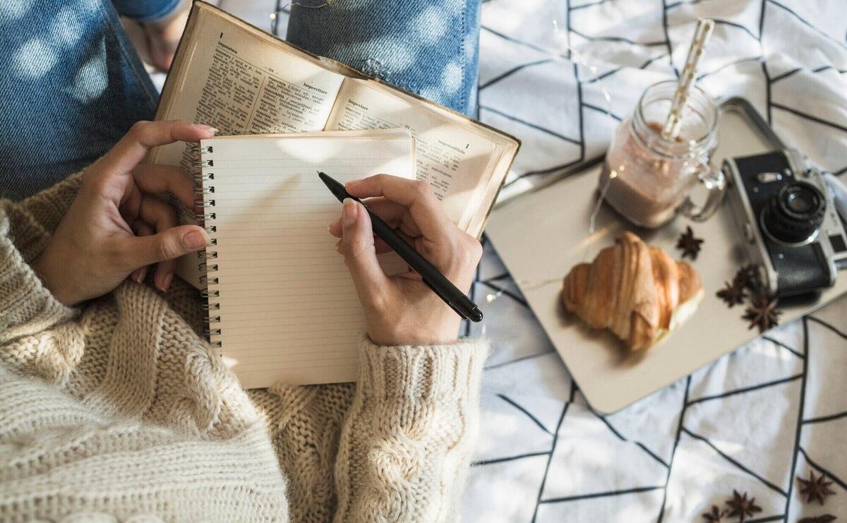 Crop woman making notes near camera and breakfast food