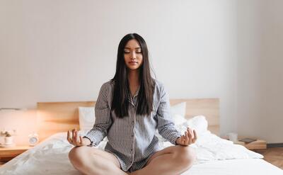 Asian woman in summer pajamas meditates sitting on white bed