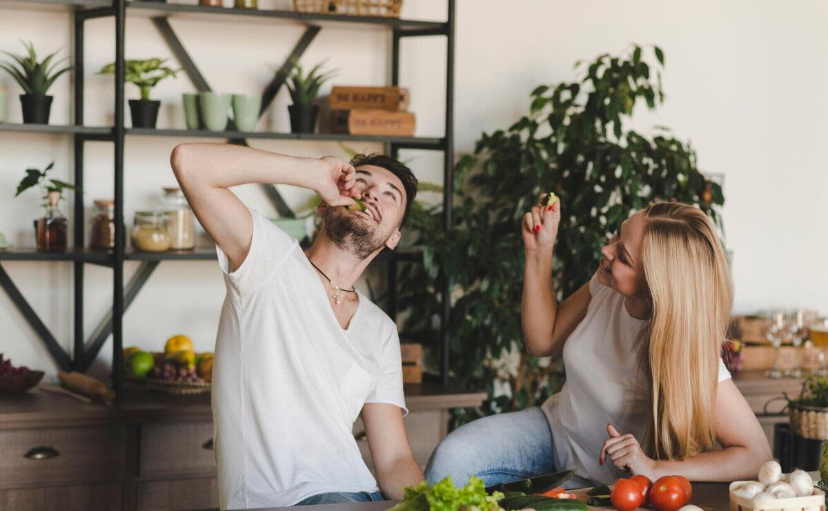 Couple sitting in the kitchen eating cucumber slice