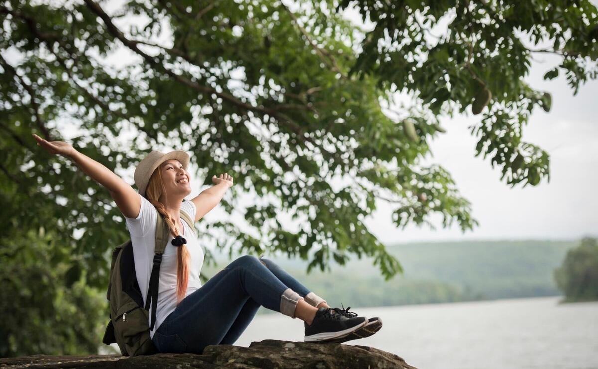 Young happy woman sitting with backpack enjoy the nature after hike.