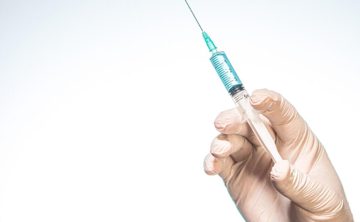 Person's hand wearing a surgical glove and holding a syringe with a white background