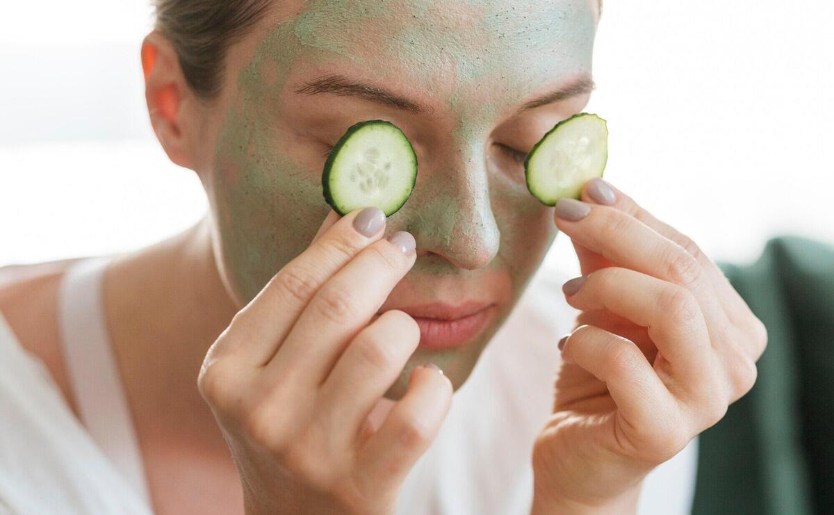 Woman with facial mask putting slices of cucumber